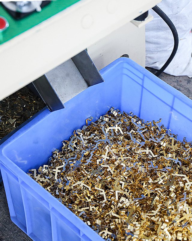 Bin of freshly stamped brass terminals beside the press